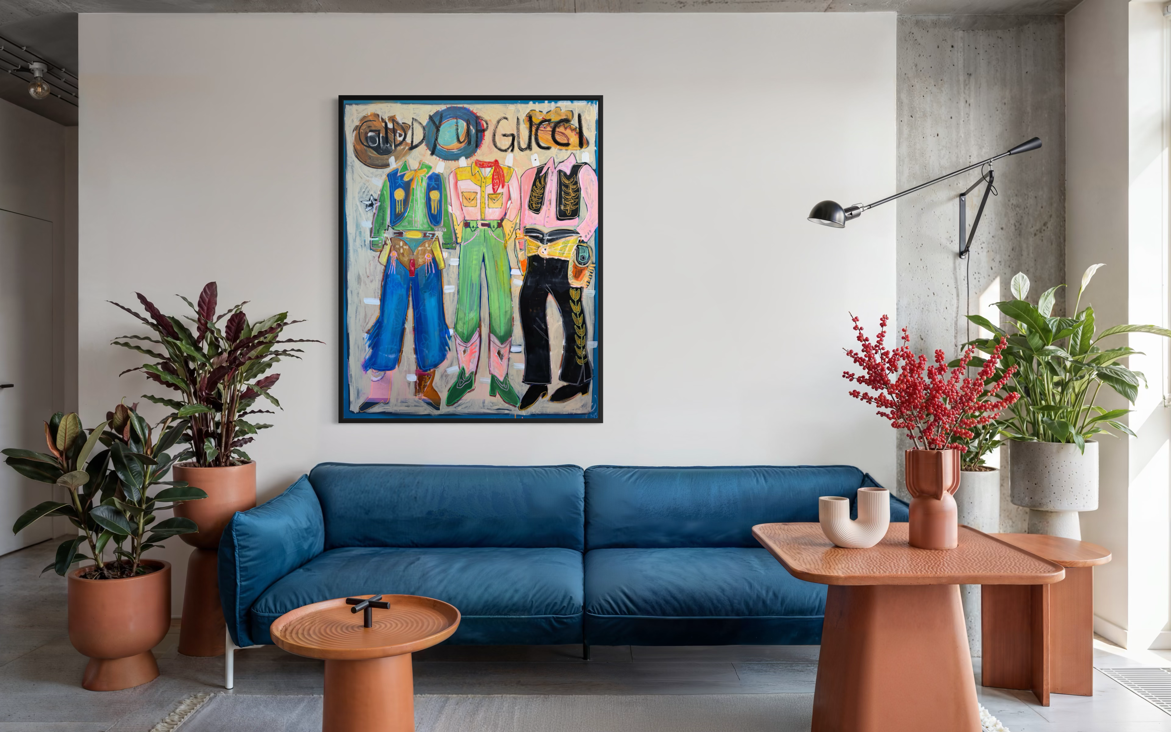 A colorful framed Gucci art featuring three stylized figures hangs on a white wall above a blue velvet sofa in a modern living room setting.